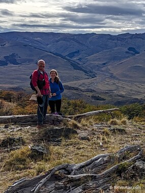 Dan and Sherry pose in front of a grassy mountain that could be in California